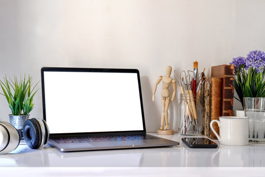 Mockup laptop on Designer desk with blank screen ,books ,coffee mug and artist supplies. artist workspace