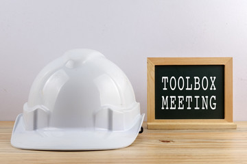 HEALTH AND SAFETY CONCEPT. Personal protective equipment on wooden table over white background with TOOLBOX MEETING text.