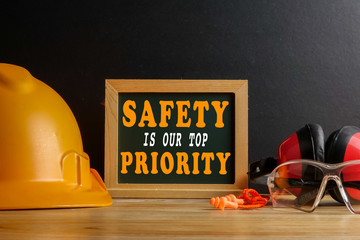 SAFETY IS OUR TOP PRIORITY CONCEPT. Personal protective equipment on wooden table over black...