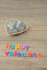 Fototapeta na wymiar A wire basket filled with silver heart shape baubles and the words happy valentine
