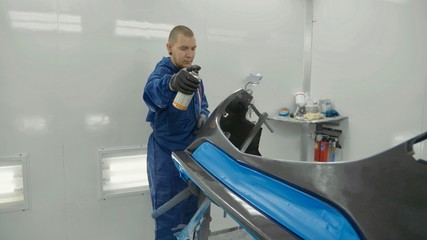 Serviceman preparing a car bodykit for painting in a workshop