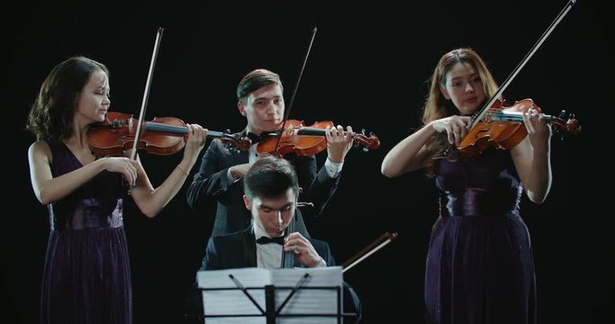 classical string quartet during the performance of the symphony, abstract black background in the studio