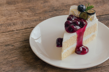 Blueberry cream cake on white plate on wood table with copy space. Vanilla sponge cake decorated with dairy whipped cream and blueberry sauce so soft sweet and delicious. Homemade bakery concept.