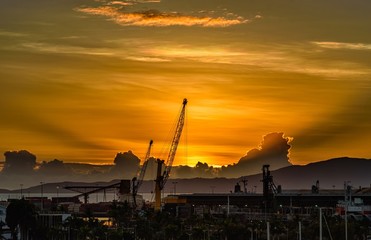 Fototapeta na wymiar A shipping crane on the docks of Townsville, Queensland, Australia is helping the sun to rise from behing a cloud.