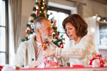 Senior couple in sweaters wrapping Christmas gifts together.