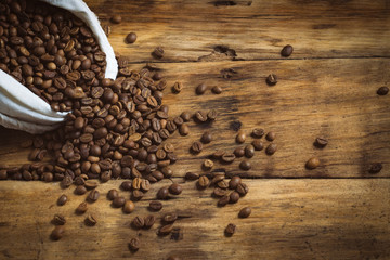 White bag with coffee beans are poured out on a wooden background. Copy space