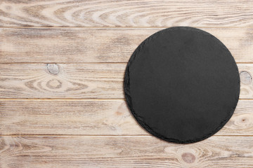 Black slate round stone on wooden background, top view, copy space