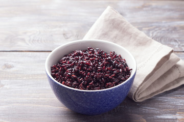 Black rice in a blue bowl on a wooden table, selective focus, rustic style. Simple healthy food