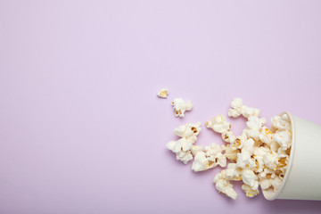 Spilled popcorn from a paper cup on a pink background, empty space for text.