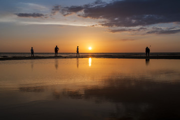 Silhouette of people strolling by the sunset on the beach with dramatic sun over the horizon