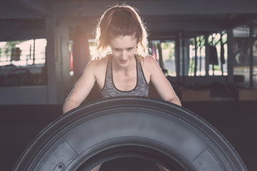 Fototapeta na wymiar Young caucasian woman exercise with big rubber tire equipment in gym. Health and fitness concept.