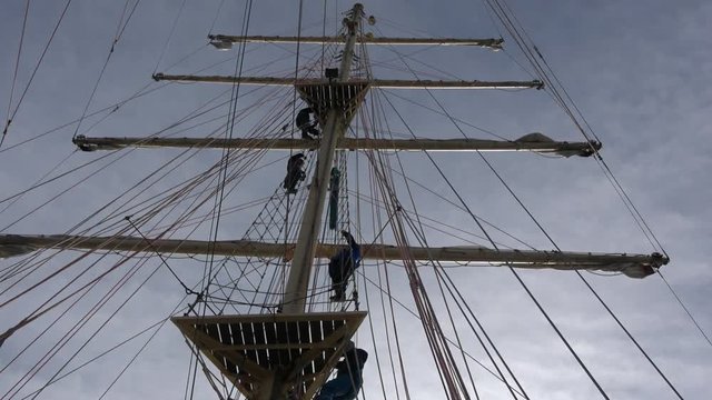 The Crew of Sailing Tall Ship is climbing the mast to enter the yards and prepare the sails. Backlight