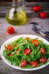fresh green salad with arugula and red tomatoes on wooden background