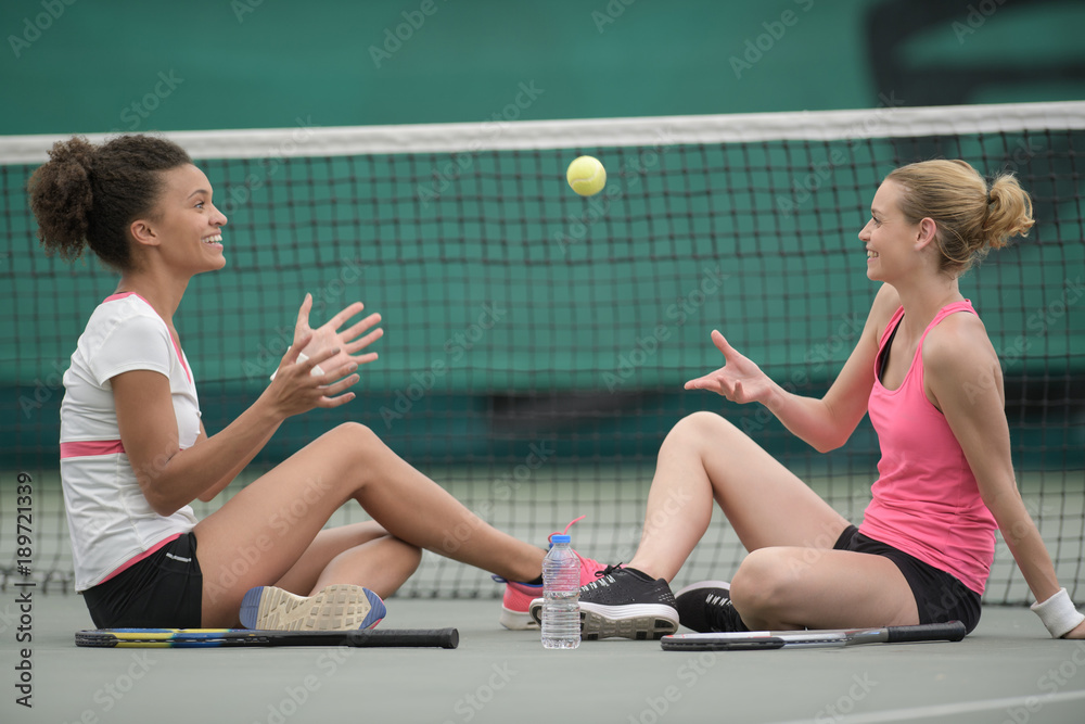 Wall mural two female tennis players sitting together on court