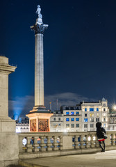 Night shot of Trafalgar Square with a girl from the back in the foreground and stars in the sky, London. - obrazy, fototapety, plakaty