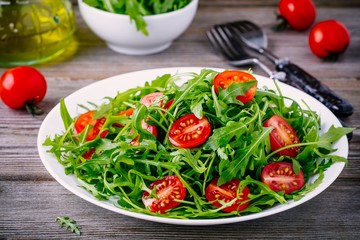 fresh green salad with arugula and red tomatoes on wooden background