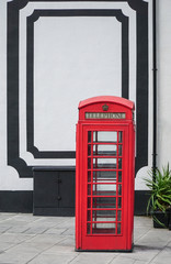 Fototapeta premium Red Telephone Box in front of a white wall in London at daylight.