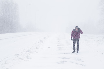 Winter is coming by snow. Poor visibility in heavy snow storm on path. Man slowly and hard walking...