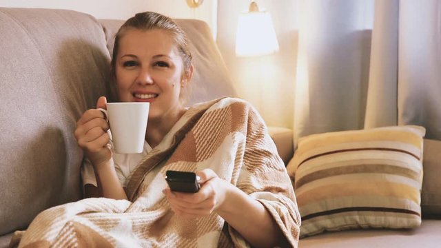 Young female is watching TV and sitting with tea at home.