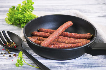 sausages in a frying pan and seasoning on a wooden background