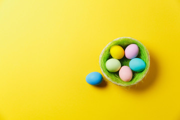 Fototapeta na wymiar Six colorful pastel monophonic painted Easter eggs in basket with green grass isolated on yellow background. Happy Easter concept. Copy space for advertisement. With place for text. Top view on eggs.