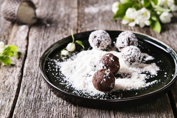 Homemade healthy vegan chocolate balls, truffles, candies sprinkled grated coconut in the plate on the vintage wooden table. Selective focus 