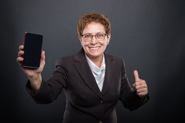Business senior lady showing smartphone and like gesture