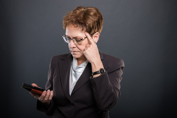 Business senior lady thinking holding smartphone