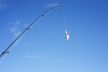 The spinning and brightly-colored crankbait are against the blue cloudless sky. The fishing...