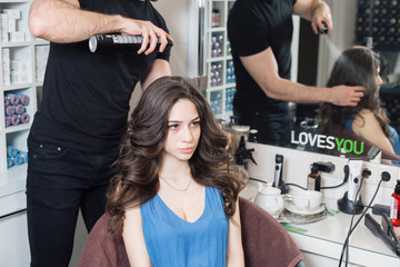 Closeup hairdresser man makes hairstyle for young woman in beauty salon