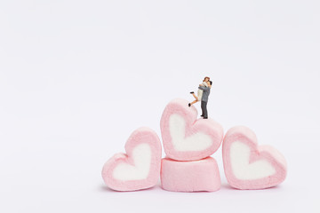 Fototapeta premium Happy miniature couple on stack on pink heart marshmallow on white background, valentine concept background