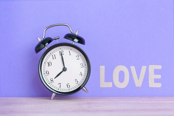 Vintage black alarm clock on purple background and word LOVE , Concept Time of Valentine day