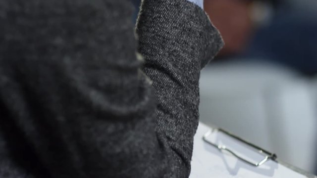 Tilt down of unrecognizable female psychotherapist listening to someone talking and writing notes on clipboard