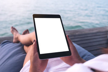 Mockup image of a woman using black tablet pc with blank white desktop screen while sitting by the sea