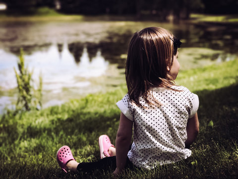 little girl sitting by a pond