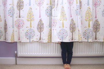 A young girl hiding behind curtains so that you can only see her legs