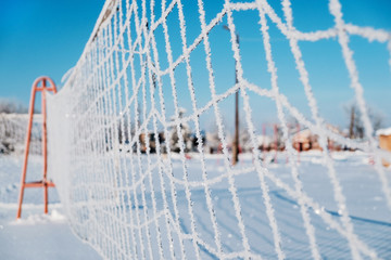 Volleyball net covered with hoarfrost. A bright winter sunny day, a cloudless blue sky.