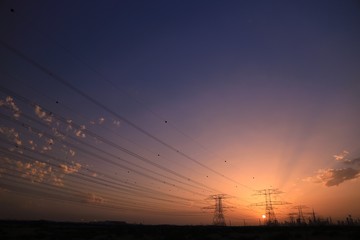 HIGH VOLTAGE PYLON WITH DUBAI SKYLINE AS BACKGROUND, INCLUDING THE LANDMARK, THE TALLEST BUILDING IN THE WORLD, BURJ KHALIFA, UNDER SUNSET