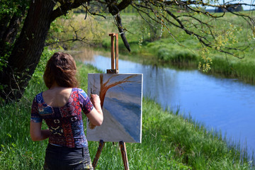 Female artist paints a beautiful small river landscape on canvas.