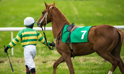 young jockey walking with his horse on the track