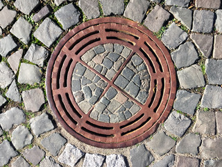 Kanaldeckel mit Pflastersteinen als Natursteinpflaster