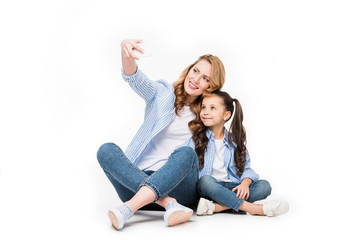 happy mother and daughter taking selfie on smartphone together isolated on white