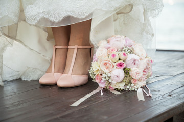 Bouquet de mariée à coté des pieds de la mariée sous sa robe