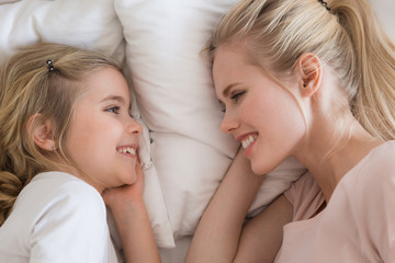top view of smiling daughter and mother lying on bed and looking at each other