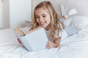 smiling kid lying on bed and reading book