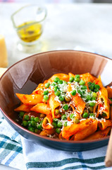 Tomato sauce and green peas penne pasta in a plate on a white stone background