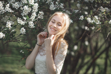 Spring beautiful romantic girl, blonde, enjoying blooming apple trees in swarn sunny day