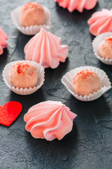 White chocolate strawberry truffles and pink meringue kisses on black stone background