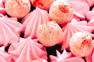 White chocolate strawberry truffles and pink meringue kisses on black stone background