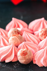 White chocolate strawberry truffles and pink meringue kisses on black stone background